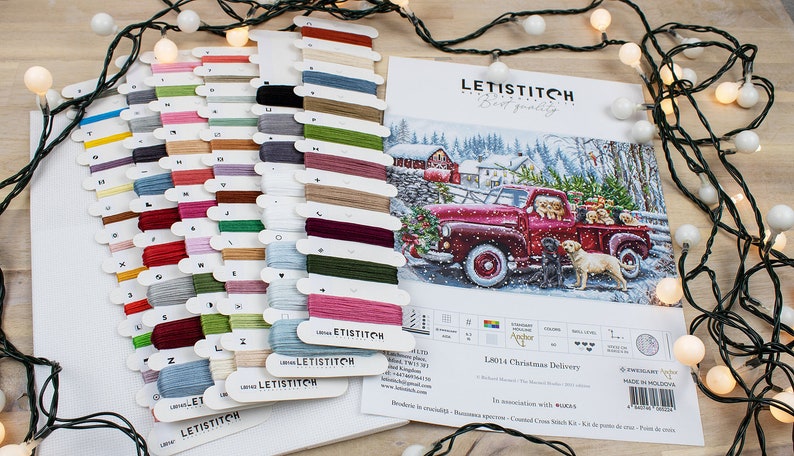 May include: A cross stitch kit featuring a red truck with a Christmas tree and dogs in the back. The kit includes a variety of colored threads and a pattern for the design. The kit is titled "L8014 Christmas Delivery".