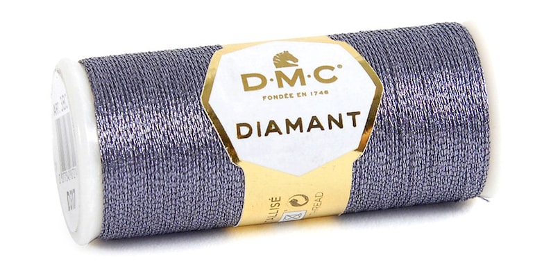 K&ouml;nnte beinhalten: Eine Spule DMC Diamant Metallic-Garn in silbergrauer Farbe. Die Spule ist mit dem DMC-Logo und dem Text "Diamant" beschriftet.