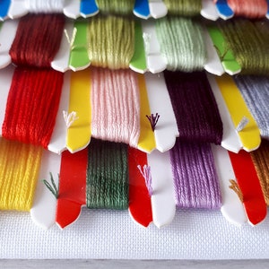 May include: A close-up of a variety of embroidery floss spools in different colors, including red, yellow, green, purple, and brown. The spools are arranged in rows and are ready for use in a craft project.