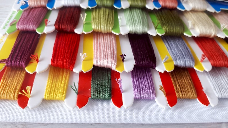 May include: A close-up of a variety of embroidery floss spools in different colors, including red, yellow, green, purple, and brown. The spools are arranged in rows and are ready for use in a craft project.