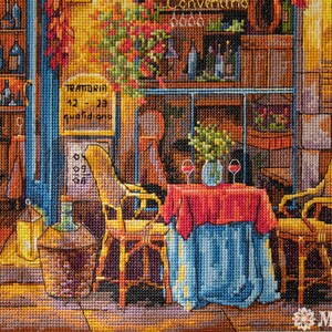 Puede incluir: Una obra de punto de cruz que representa una acogedora escena de restaurante italiano con un mantel rojo y azul, dos sillas y una copa de vino sobre la mesa. El letrero sobre la puerta dice "TRATTORIA 12 - 23 quotidiano".