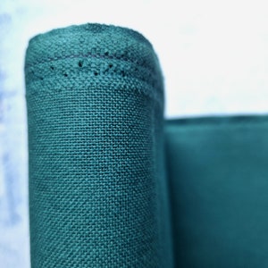 以下が含まれることがあります： ステッチの付いた端で巻かれたティールグリーンの生地のクローズアップ。