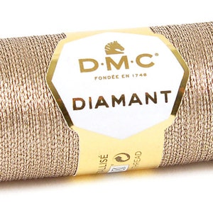 Puede incluir: Una bobina de hilo metálico DMC Diamant de color dorado. La bobina está etiquetada con el logotipo de DMC y el texto "Diamant".