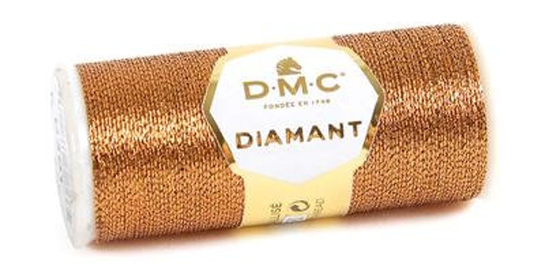 K&ouml;nnte beinhalten: Eine Spule goldfarbener Metallic-Garn mit der Aufschrift "DMC Diamant", einem Pferdekopf-Logo und dem Text "Fondee en 1790".