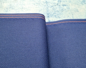 May include: Close-up of two folded sections of blue fabric with a woven texture. The edges are trimmed with a thin orange stripe. The background is a light blue and white mottled surface.