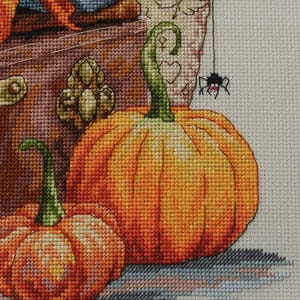 May include: A cross-stitch embroidery design featuring two orange pumpkins with green stems, a small black spider hanging from a thread, and a textured brown background. The word Merejka is printed in white in the bottom right corner of the fabric.