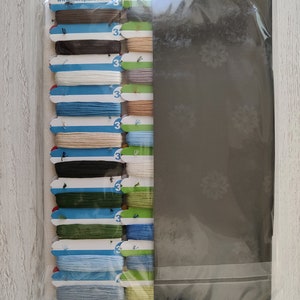 K&ouml;nnte beinhalten: Ein Set mit 16 Stickgarnrollen in verschiedenen Farben, darunter Braun, Blau, Gr&uuml;n und Beige. Die Rollen sind in einer Reihe angeordnet und mit der Nummer "3" gekennzeichnet. Die Rollen sind in einer durchsichtigen Plastikt&uuml;te mit wei&szlig;em Hintergrund verpackt. Die T&uuml;te enth&auml;lt auch eine wei&szlig;e Karte mit dem Text "Merejka" und der Website-Adresse "www.merejka.com". Auf der R&uuml;ckseite der T&uuml;te steht der Text "Alle Rechte vorbehalten &copy; Merejka, Hergestellt in Polen."