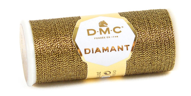 K&ouml;nnte beinhalten: Eine Spule goldfarbener Metallic-Garn mit der Aufschrift "DMC Diamant", dem DMC-Logo und "Fondee en 1746".