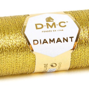 K&ouml;nnte beinhalten: Eine Spule goldfarbener Metallic-Garn mit der Aufschrift "DMC Diamant", dem DMC-Logo und dem Text "Fondee en 1746".