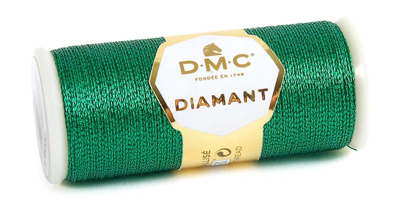 K&ouml;nnte beinhalten: Eine Spule mit gr&uuml;nem Metallic-Garn mit einem goldenen Etikett, auf dem "D.M.C. Fond&eacute;e en 1748 Diamant" steht.