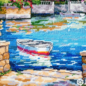 K&ouml;nnte beinhalten: Eine Kreuzstich-Stickerei, die ein kleines Boot zeigt, das in einem blauen Gew&auml;sser angedockt ist. Das Boot ist wei&szlig; mit einem roten und gelben Streifen. Die Szene wird von Steinmauern und &uuml;ppigem Gr&uuml;n eingerahmt.