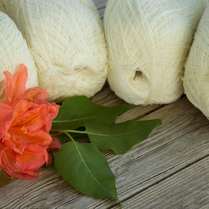May include: Four balls of white yarn with a single orange flower in the foreground.