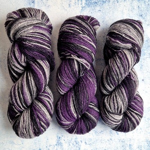 Puede incluir: Tres ovillos de hilo en un patrón de rayas de color morado, negro y gris.