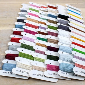 May include: A collection of embroidery floss spools organized by color and labeled with letters. The spools are arranged in rows and are all from the same brand, Letistitch.