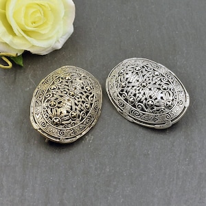 Può includere: Due spille ovali con intricati disegni di nodi celtici. Una spilla è d'argento e l'altra d'oro.