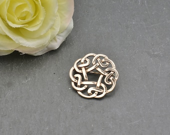 May include: A gold-toned Celtic knot brooch with a circular design. The knot is intricate and detailed, with a five-pointed star shape in the center.