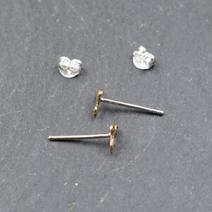 May include: A pair of silver earring backs and two gold stud earrings with a small, decorative design.