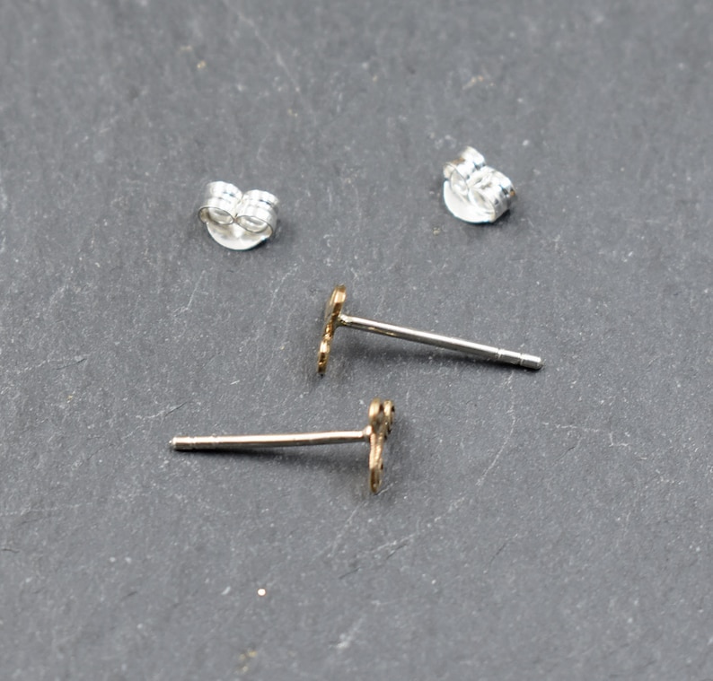 May include: A pair of silver earring backs and two gold stud earrings with a small, decorative design.