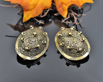 May include: Two gold-toned metal decorative pieces with intricate designs and raised dots. The pieces are oval shaped and have a textured surface.