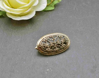 Puede incluir: Un broche ovalado de color dorado con un diseño intrincado y calado. El diseño presenta una cruz central con patrones en espiral y nudos.