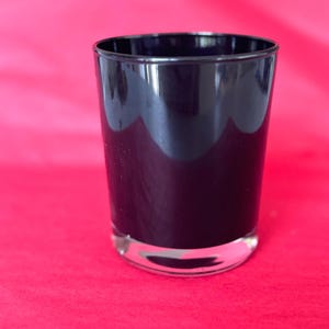 Può includere: Un bicchiere di vetro nero con fondo trasparente. Il bicchiere è vuoto e si trova su una superficie rosa.