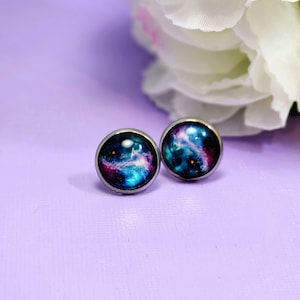 May include: A pair of silver stud earrings with a galaxy design. The galaxy is a swirling mix of blue, purple, and pink.