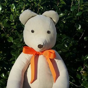 May include: Cream-colored teddy bear with brown button eyes and a brown nose. The bear has an orange ribbon tied in a bow around its neck. The bear's feet are brown with the words "Love Papa" and "Easton" embroidered on them.