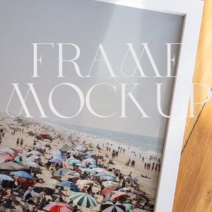 以下が含まれることがあります： 白いフレームに入ったビーチの風景。画像には、カラフルな傘、人々、そして明るいフォントで「FRAME MOCKUP」というテキストが表示された、混雑したビーチが写っています。