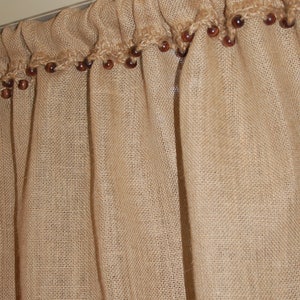May include: A brown burlap valance with a crocheted trim and brown wooden beads.