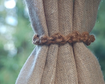 May include: A close-up of a burlap curtain tied with a thick brown rope. The rope is braided and has a rustic look.