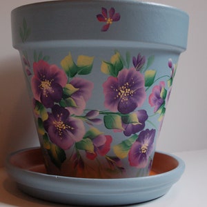 May include: A light blue ceramic planter with a hand-painted design of purple and pink flowers with green leaves.
