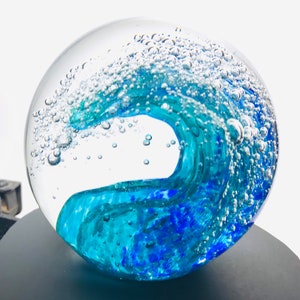 May include: A glass paperweight with a blue and green wave design and air bubbles inside.