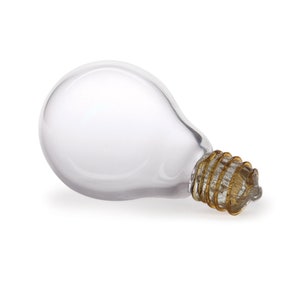 May include: A clear glass light bulb with a gold-colored metal base. The bulb is lying on its side.
