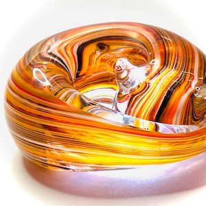 May include: A glass sculpture in the shape of a curled-up animal, with swirling stripes of white, orange, yellow, and brown glass.