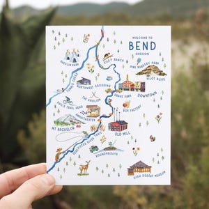 May include: A watercolor illustration of a map of Bend, Oregon. The map features landmarks like Shevlin Park, Tumalo Creek, Riley Ranch, Drake Park, Pilot Butte, and the Old Mill. The map is surrounded by a blue border and has a white background.
