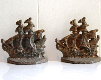 May include: Two bronze-colored ship bookends. Each bookend features a detailed depiction of a sailing ship with multiple masts and sails. The bookends are designed to stand upright and are likely made of cast metal.
