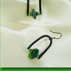 May include: A pair of black wire earrings with green and gold beads and a green and black patterned charm.