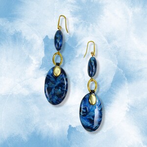 May include: A pair of dangle earrings with blue and gold oval-shaped beads. The beads have a marbled pattern.