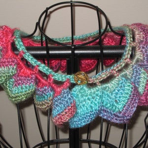 May include: A crocheted collar with a colorful, multi-colored design in shades of pink, green, blue, and purple. The collar has a decorative metal button in the center.
