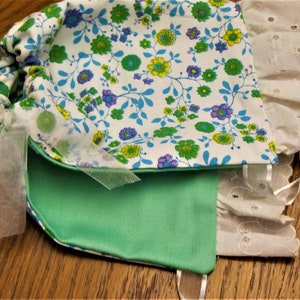 Puede incluir: Una bolsa de tela verde y blanca con estampado floral y ribete de encaje blanco. La bolsa tiene un cierre de cord&oacute;n y una cinta blanca atada alrededor.