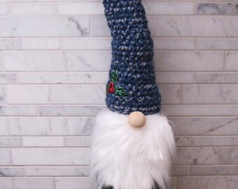 May include: A decorative gnome bottle topper. The gnome has a long, curved blue and gray crocheted hat with a small holly accent. A white faux fur beard and a wooden nose sit above the bottle of Martinelli's Sparkling Cider.