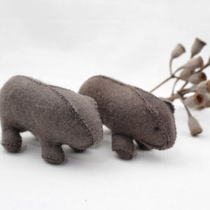 Könnte beinhalten: Zwei graue Filz-Wombats, die nebeneinander auf einer weißen Oberfläche stehen.