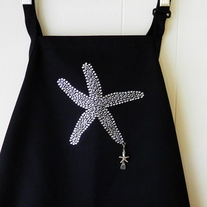 May include: Black apron with a rhinestone starfish design and a silver starfish charm hanging from the bottom.