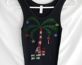 May include: Black tank top with a palm tree design covered in rhinestones. The palm tree is decorated with red and white candy cane stripes, green leaves, and colorful ornaments. The tree is also decorated with a red star and a gift box.