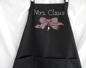May include: Black apron with a large red and white rhinestone bow and the text "Mrs. Claus" in rhinestones.