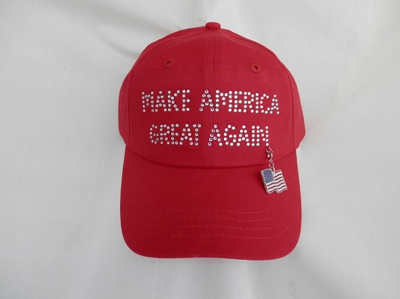 Pu&ograve; includere: Un cappellino da baseball rosso con la scritta "MAKE AMERICA GREAT AGAIN" in strass. Un piccolo ciondolo a forma di bandiera americana pende dalla visiera.
