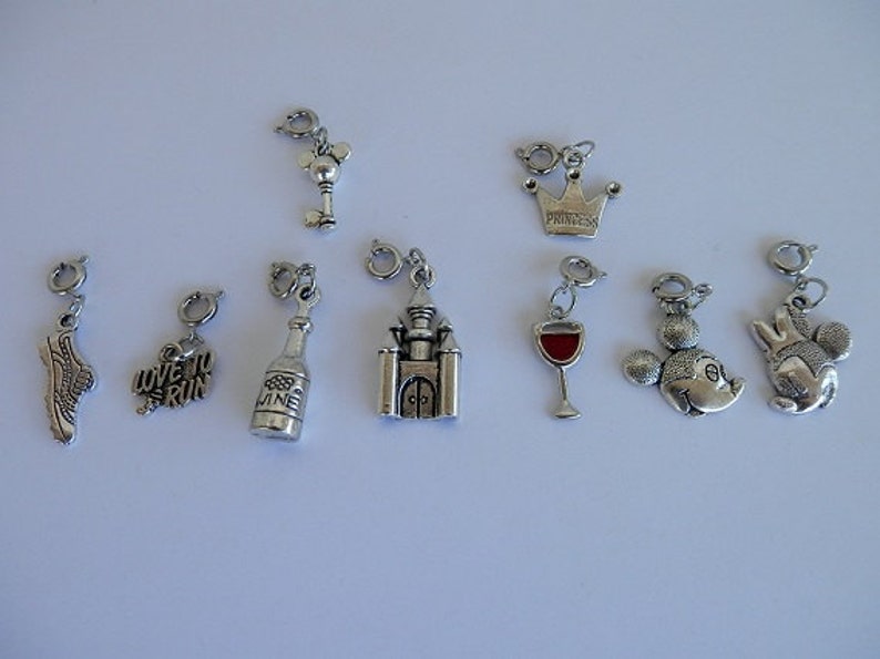 May include: A set of ten silver charm pendants, including a wine bottle, a running shoe, a castle, a wine glass, a key, a crown with the word "Princess" on it, and two Mickey Mouse heads.