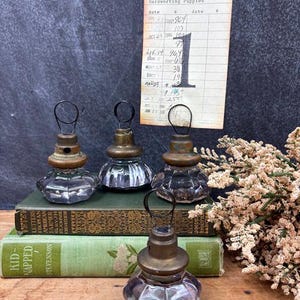 May include: Four clear glass, faceted, hexagonal-shaped card holders with brass-toned metal tops and black wire loops. A vintage library card labeled Reiser, Lynn and Hardworking Puppies is held upright by one of the glass and brass holders.