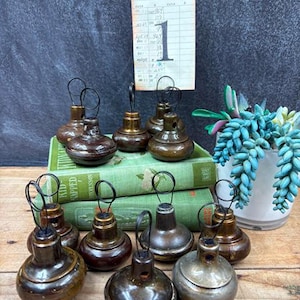 May include: A collection of vintage-style metal ornaments in various shades of brown and gold, each with a small loop for hanging. The ornaments are arranged on a wooden surface with a stack of green books and a decorative succulent plant.