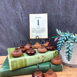 May include: A collection of wooden photo holders with a dark brown finish and wire loops. The holders are arranged on top of two vintage green books. A calendar page shows "Thursday, July 1".